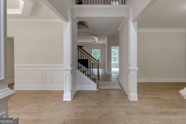 foyer entrance with decorative columns, ornamental molding, stairs, light wood-type flooring, and a decorative wall