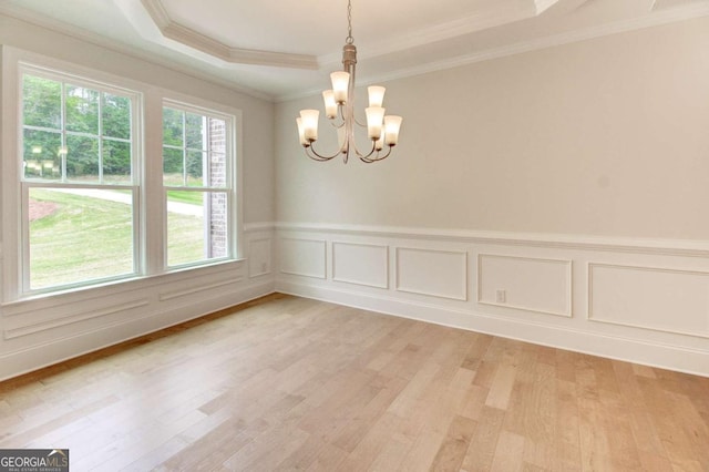 spare room with wainscoting, light wood finished floors, an inviting chandelier, a raised ceiling, and crown molding