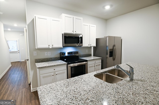 kitchen with stainless steel appliances, white cabinetry, sink, and light stone countertops