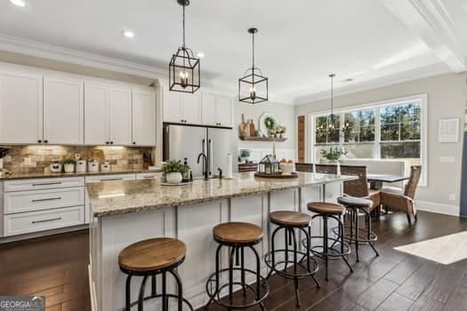 kitchen featuring white cabinets, pendant lighting, an island with sink, and dark wood-type flooring