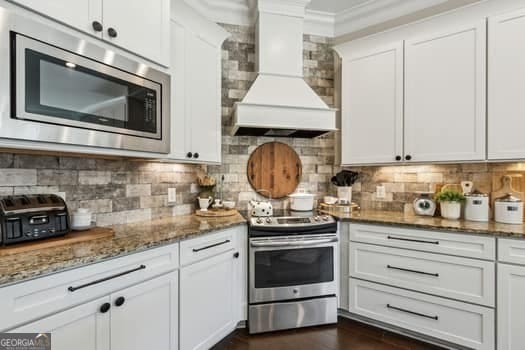 kitchen with custom exhaust hood, stainless steel appliances, decorative backsplash, white cabinetry, and stone counters