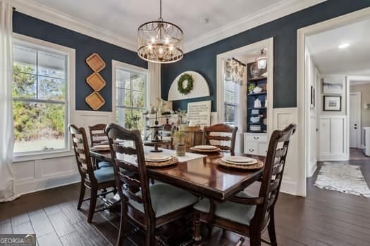 dining room with dark wood-type flooring, an inviting chandelier, ornamental molding, and a wealth of natural light