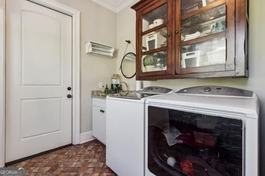 laundry area featuring washer and clothes dryer, ornamental molding, and cabinets