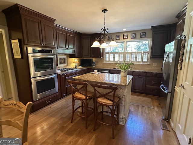 kitchen with light hardwood / wood-style floors, a center island, dark brown cabinetry, light stone countertops, and stainless steel appliances