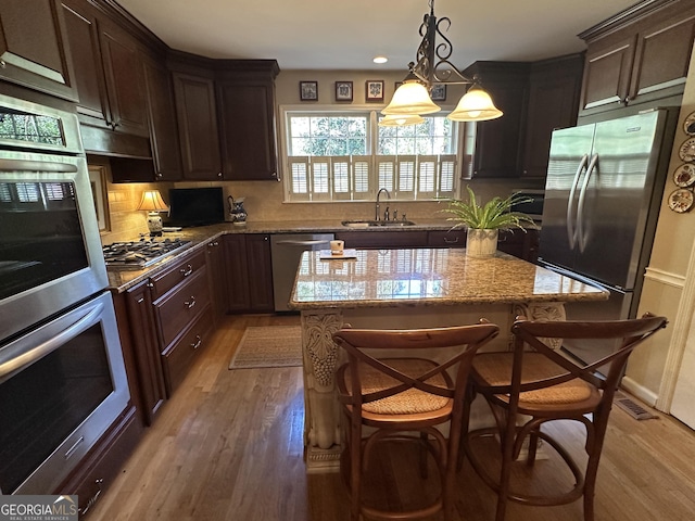 kitchen featuring a kitchen island, a kitchen bar, sink, light stone countertops, and appliances with stainless steel finishes