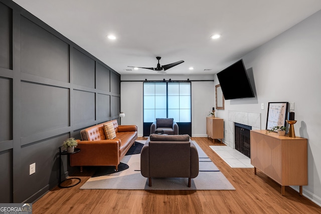 living room with a tiled fireplace, ceiling fan, and light hardwood / wood-style flooring