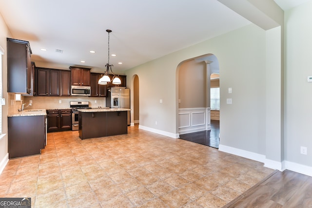 kitchen with decorative light fixtures, stainless steel appliances, decorative backsplash, a kitchen island, and sink