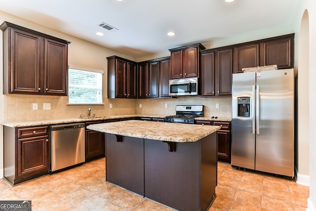 kitchen with stainless steel appliances, a breakfast bar, tasteful backsplash, a kitchen island, and sink