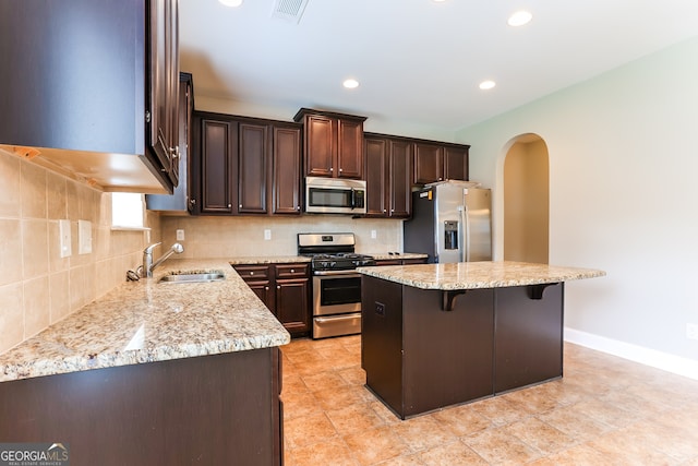 kitchen with light stone countertops, a center island, a breakfast bar area, appliances with stainless steel finishes, and sink