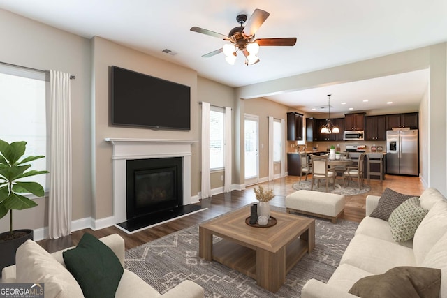 living room featuring ceiling fan with notable chandelier and dark wood-type flooring