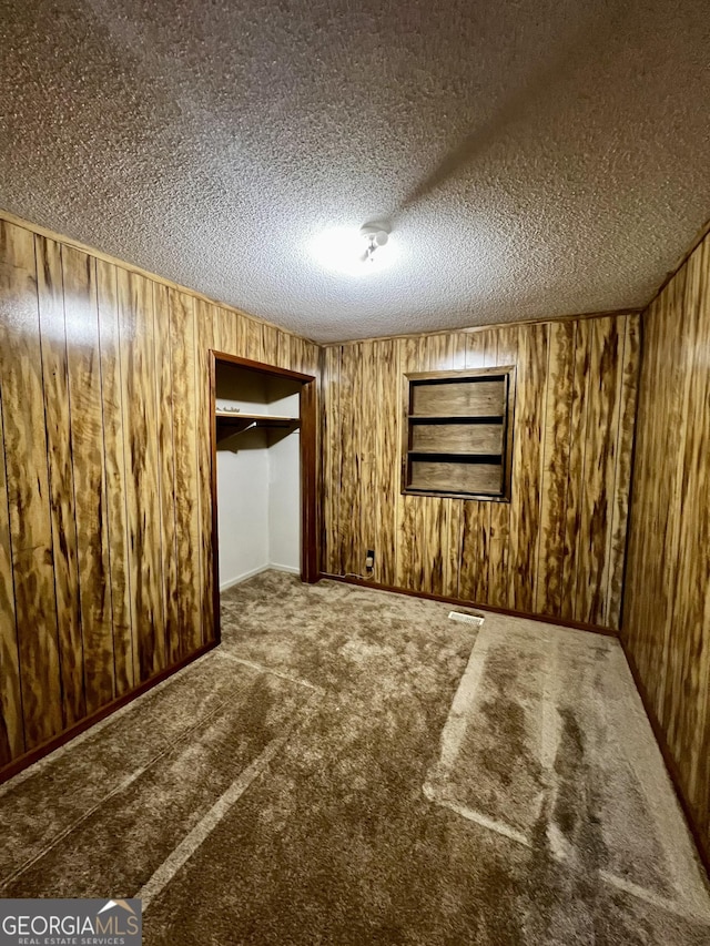 unfurnished bedroom featuring a textured ceiling, wooden walls, a closet, and carpet