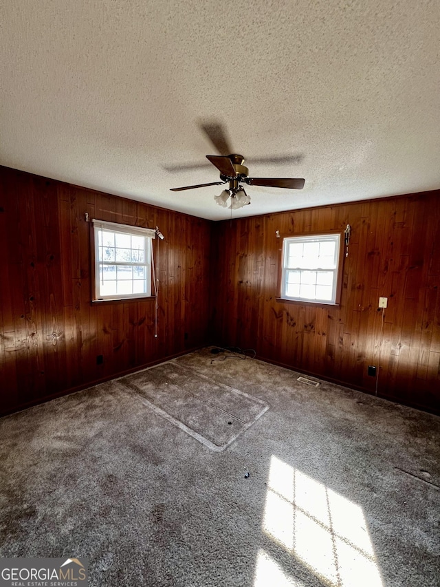 carpeted empty room with a textured ceiling, ceiling fan, and wood walls