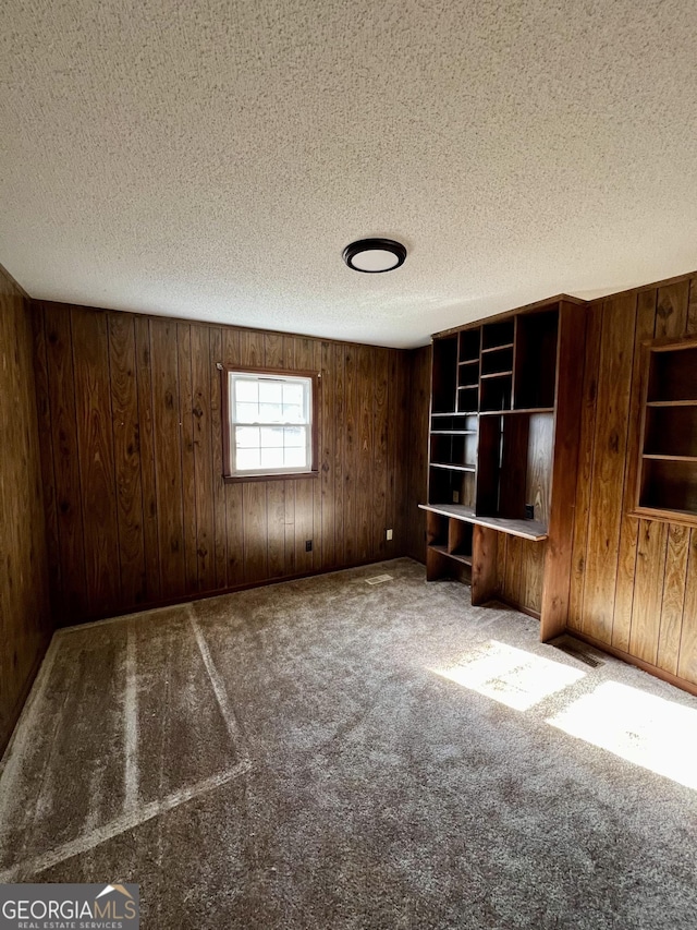 interior space featuring a textured ceiling, wooden walls, and carpet