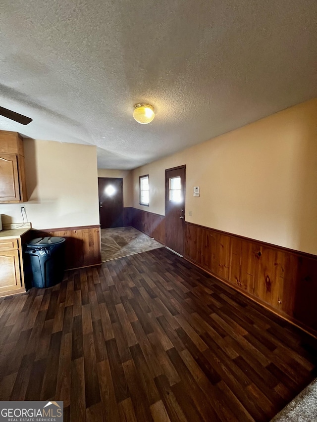 interior space with a textured ceiling, wooden walls, and dark hardwood / wood-style floors