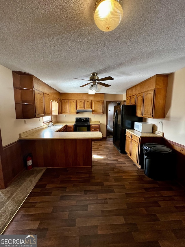 kitchen featuring kitchen peninsula, wood walls, black appliances, dark hardwood / wood-style flooring, and ceiling fan