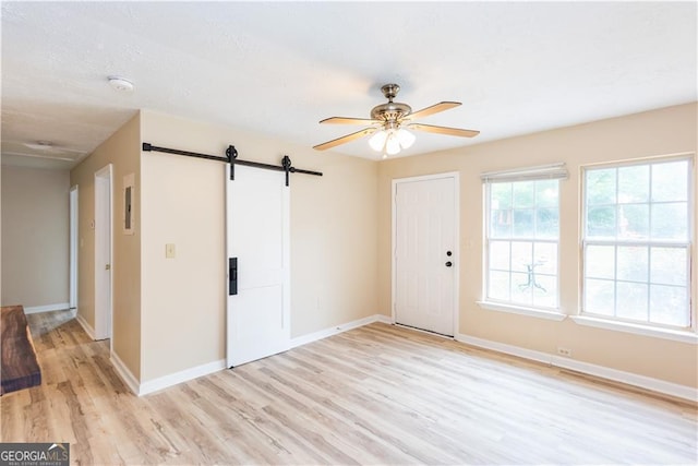 unfurnished room featuring ceiling fan, a barn door, and light hardwood / wood-style floors