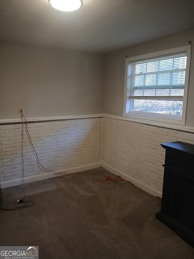 unfurnished room featuring carpet floors, a wainscoted wall, and brick wall