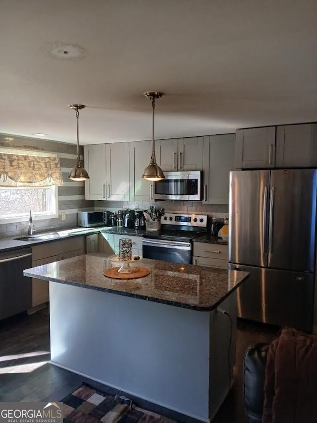 kitchen with stainless steel appliances, backsplash, gray cabinetry, a sink, and dark stone countertops