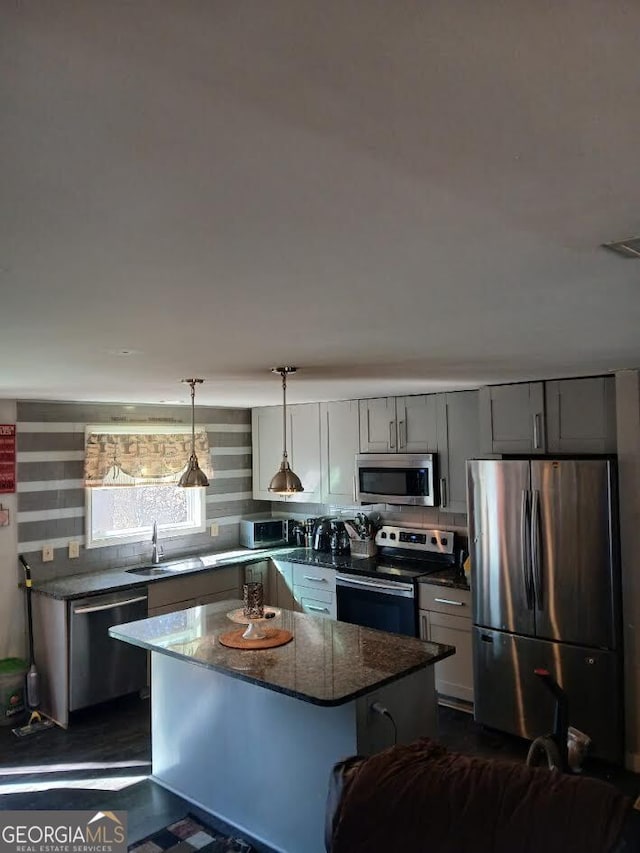 kitchen featuring a center island, stainless steel appliances, gray cabinetry, a sink, and dark stone counters