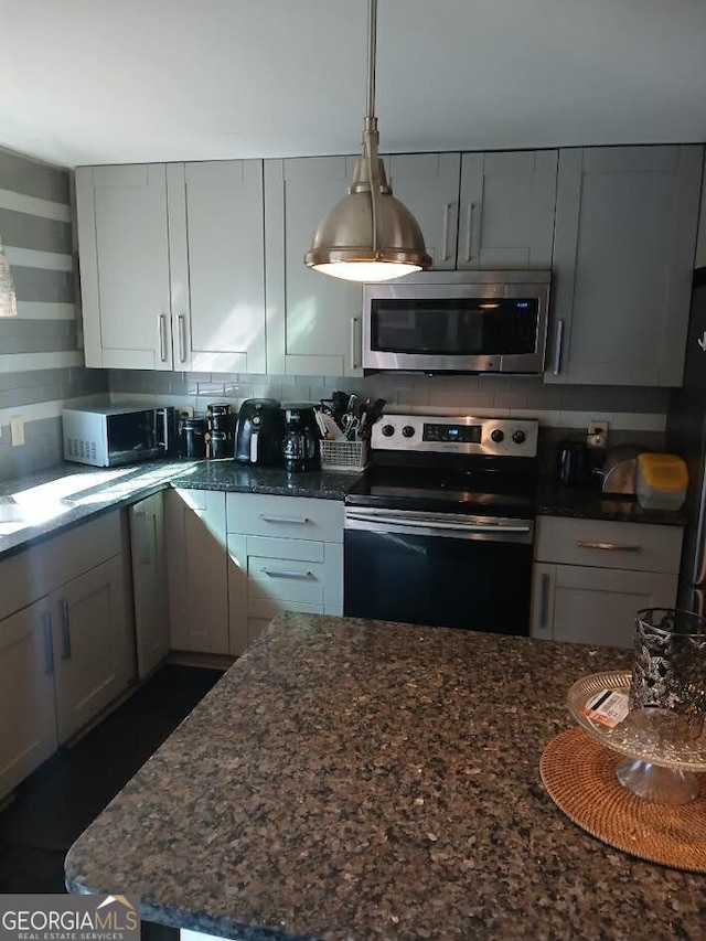 kitchen featuring dark stone counters, stainless steel appliances, hanging light fixtures, and decorative backsplash