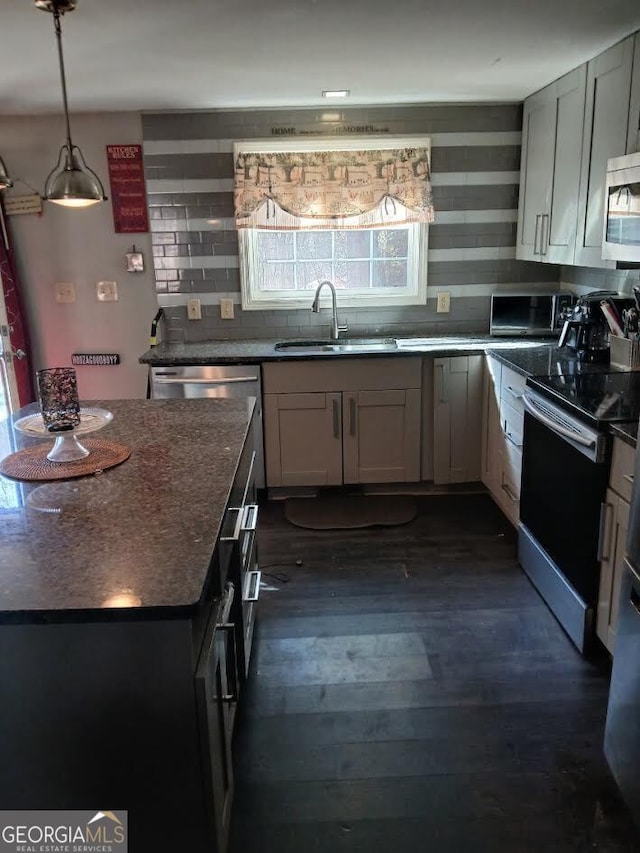 kitchen featuring dark wood finished floors, tasteful backsplash, appliances with stainless steel finishes, a sink, and dark stone countertops