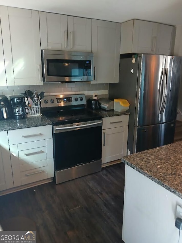 kitchen with appliances with stainless steel finishes, dark stone counters, dark wood finished floors, and backsplash