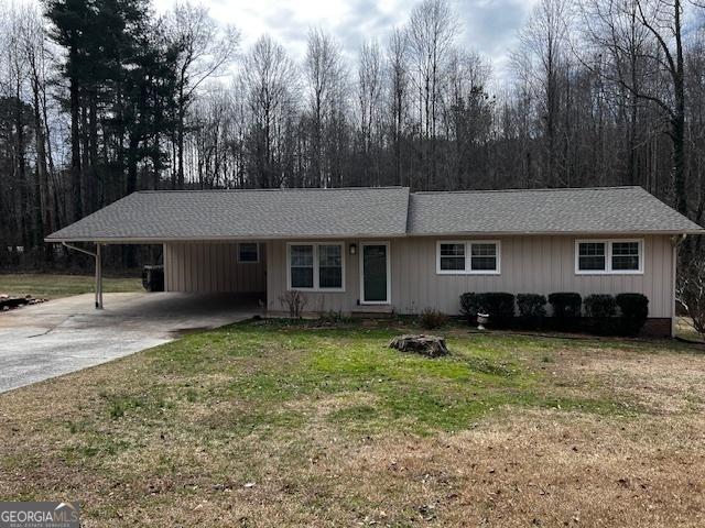 ranch-style home featuring driveway, an attached carport, roof with shingles, board and batten siding, and a front yard