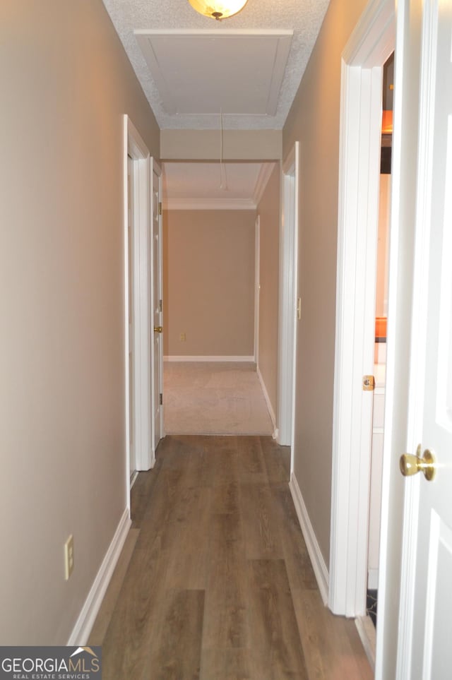 hallway featuring attic access, a textured ceiling, baseboards, and wood finished floors