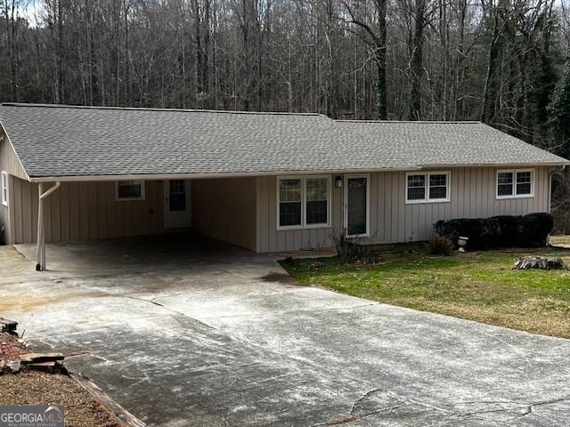 ranch-style home featuring a front lawn, an attached carport, concrete driveway, and roof with shingles