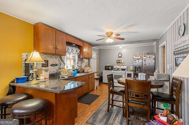 kitchen with stainless steel fridge, light hardwood / wood-style flooring, a textured ceiling, white range with gas cooktop, and kitchen peninsula