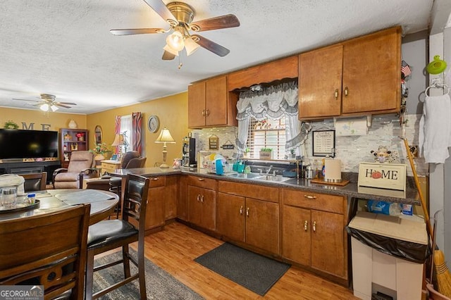 kitchen with sink, light wood-type flooring, backsplash, ceiling fan, and a textured ceiling