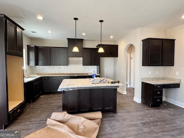 kitchen featuring backsplash, light stone countertops, a kitchen island, pendant lighting, and dark wood-type flooring