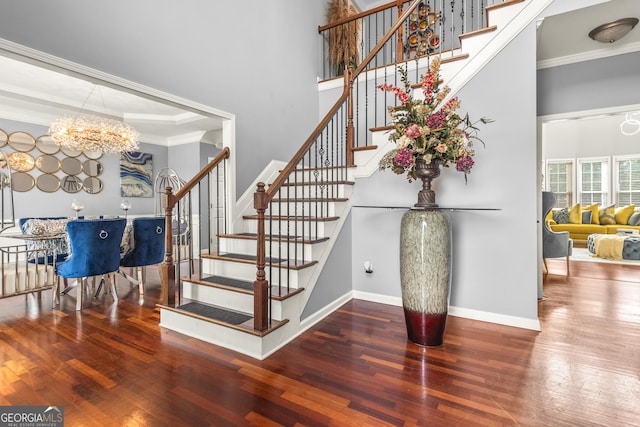 stairway featuring a high ceiling, an inviting chandelier, hardwood / wood-style floors, and crown molding