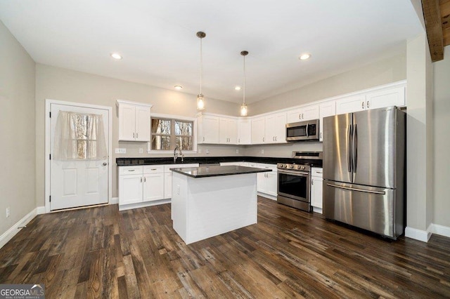 kitchen with appliances with stainless steel finishes, decorative light fixtures, white cabinetry, a kitchen island, and dark wood-type flooring