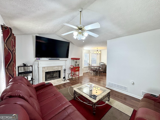 living room with vaulted ceiling, a textured ceiling, dark hardwood / wood-style floors, a fireplace, and ceiling fan with notable chandelier