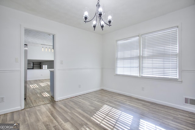 unfurnished room featuring a notable chandelier and light hardwood / wood-style floors