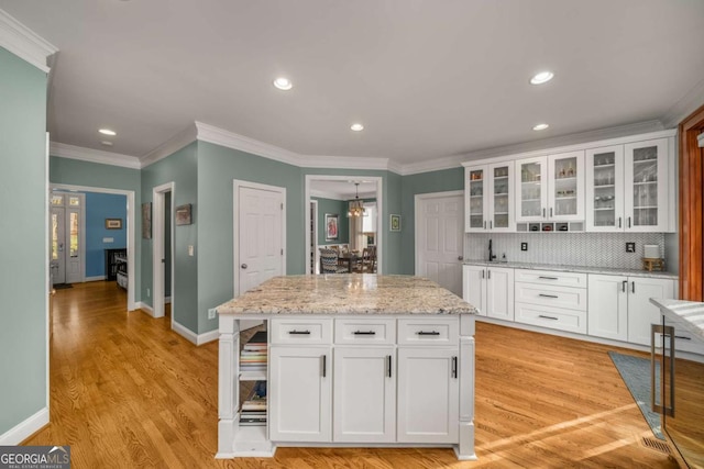 kitchen featuring ornamental molding, light stone counters, a kitchen island, white cabinets, and tasteful backsplash