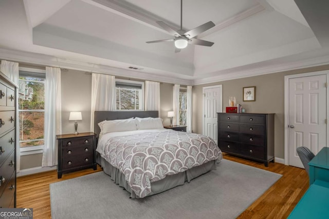 bedroom featuring hardwood / wood-style flooring, a raised ceiling, ceiling fan, and crown molding