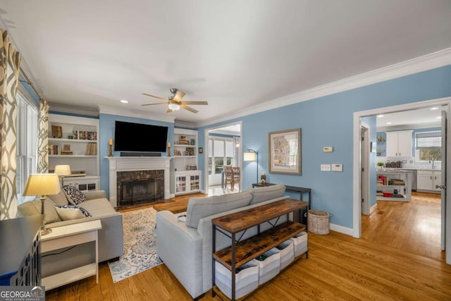 living room with light hardwood / wood-style flooring, crown molding, a high end fireplace, built in features, and ceiling fan