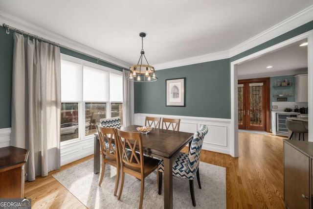 dining room with beverage cooler, an inviting chandelier, ornamental molding, and light hardwood / wood-style flooring