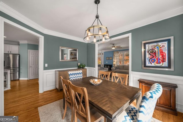 dining space featuring light hardwood / wood-style flooring, crown molding, and ceiling fan with notable chandelier