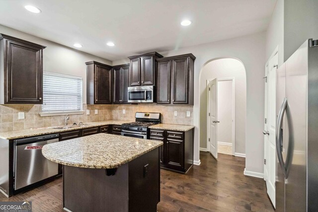 kitchen featuring appliances with stainless steel finishes, a center island, dark wood-type flooring, light stone counters, and sink