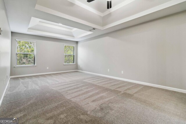 empty room featuring ceiling fan, light colored carpet, and a raised ceiling