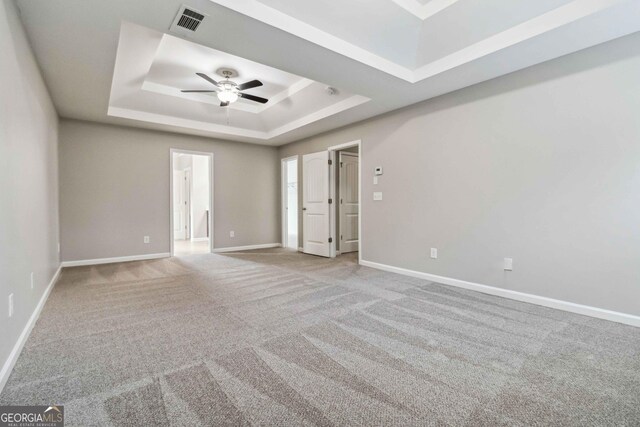 empty room featuring light carpet, ceiling fan, and a tray ceiling