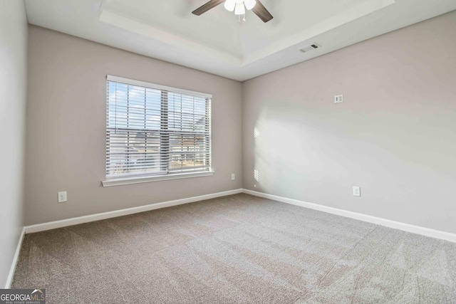 carpeted spare room with a raised ceiling and ceiling fan