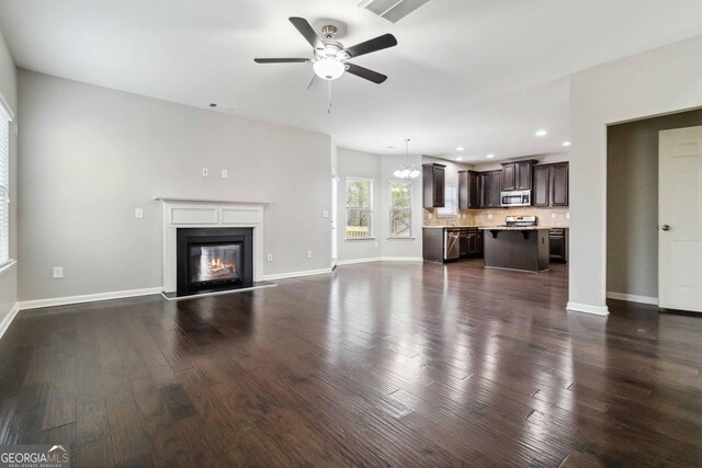 unfurnished living room with ceiling fan with notable chandelier and dark hardwood / wood-style flooring