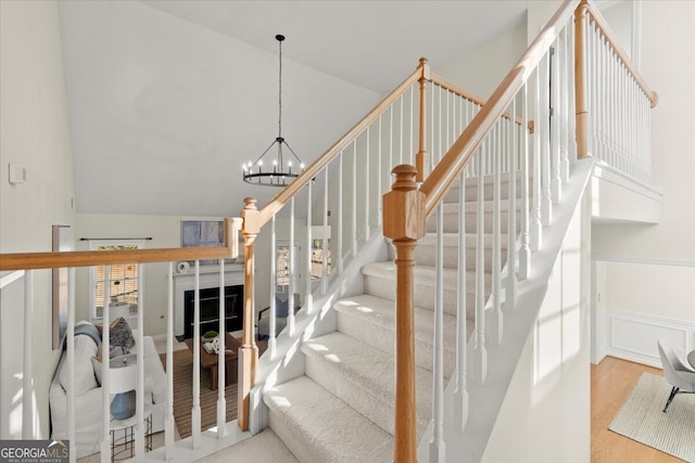 staircase with vaulted ceiling, a notable chandelier, and hardwood / wood-style floors