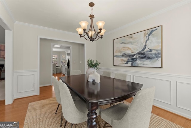 dining area with light wood-type flooring, ornamental molding, and a chandelier