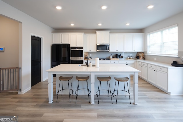 kitchen featuring white cabinetry, an island with sink, a breakfast bar area, and black appliances