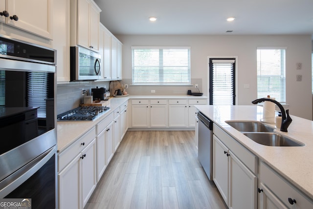 kitchen featuring appliances with stainless steel finishes, sink, backsplash, white cabinets, and light wood-type flooring